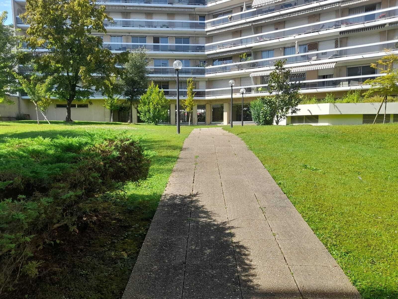 Een pad dat leidt naar een meerlaags gebouw met balkons, omgeven door groen en bomen.