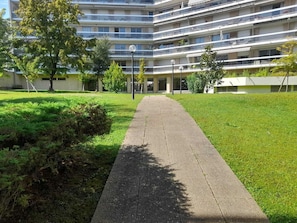 Een pad dat leidt naar een meerlaags gebouw met balkons, omgeven door groen en bomen.