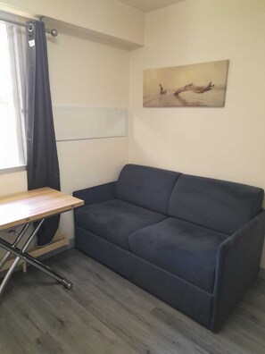 Ett rum med en mörkblå soffa, ett träbord och en tavla på väggen.