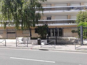 En byggnad med en sluten entré, en platt fasad, ett staket av metall och ett träd i förgrunden.