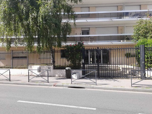 Un immeuble clos, doté d’une façade plate, d’une clôture en métal et d’un arbre au premier plan.