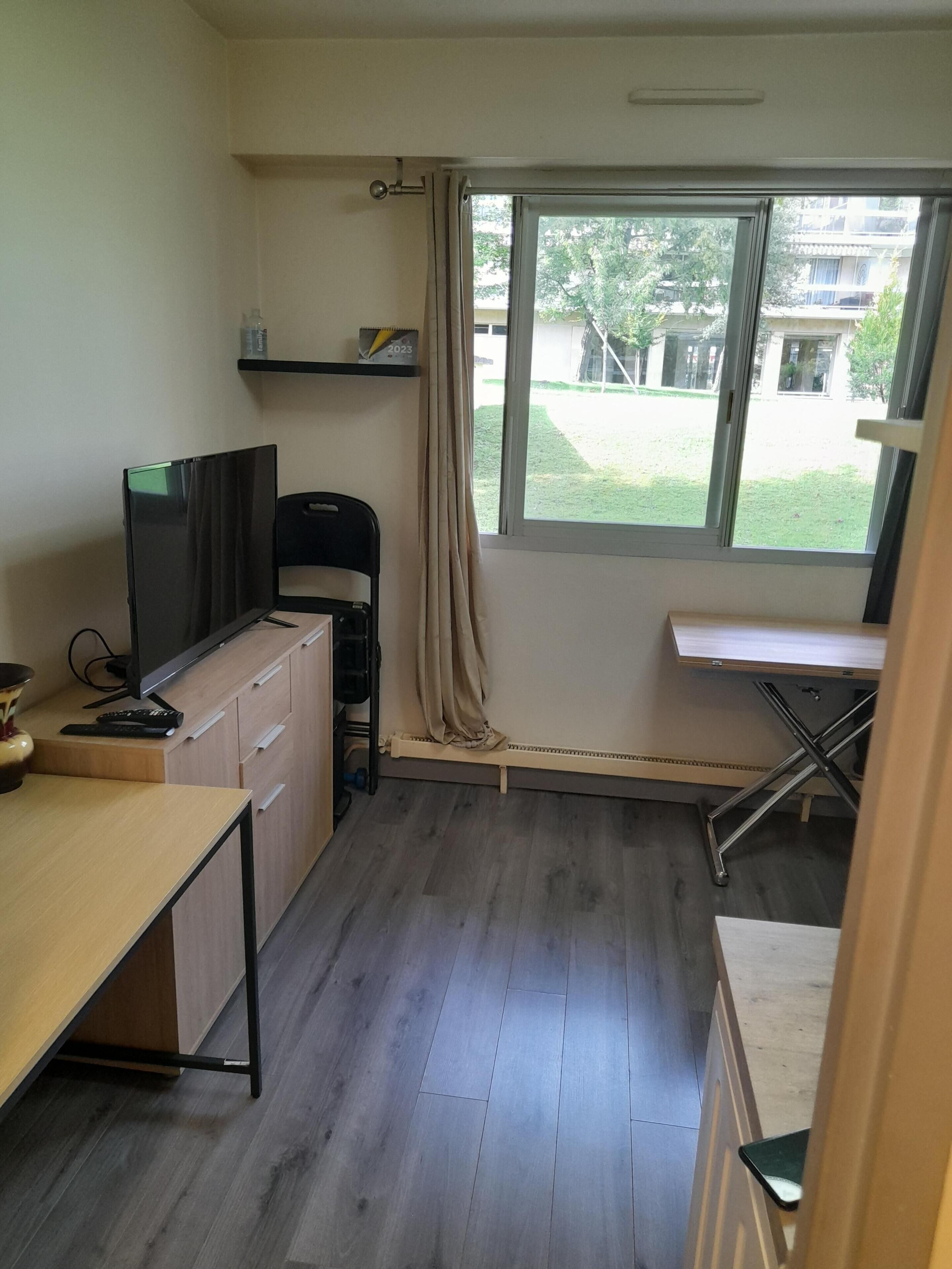 Een ruime, goed verlichte kamer met een bureau, stoel en groot raam.