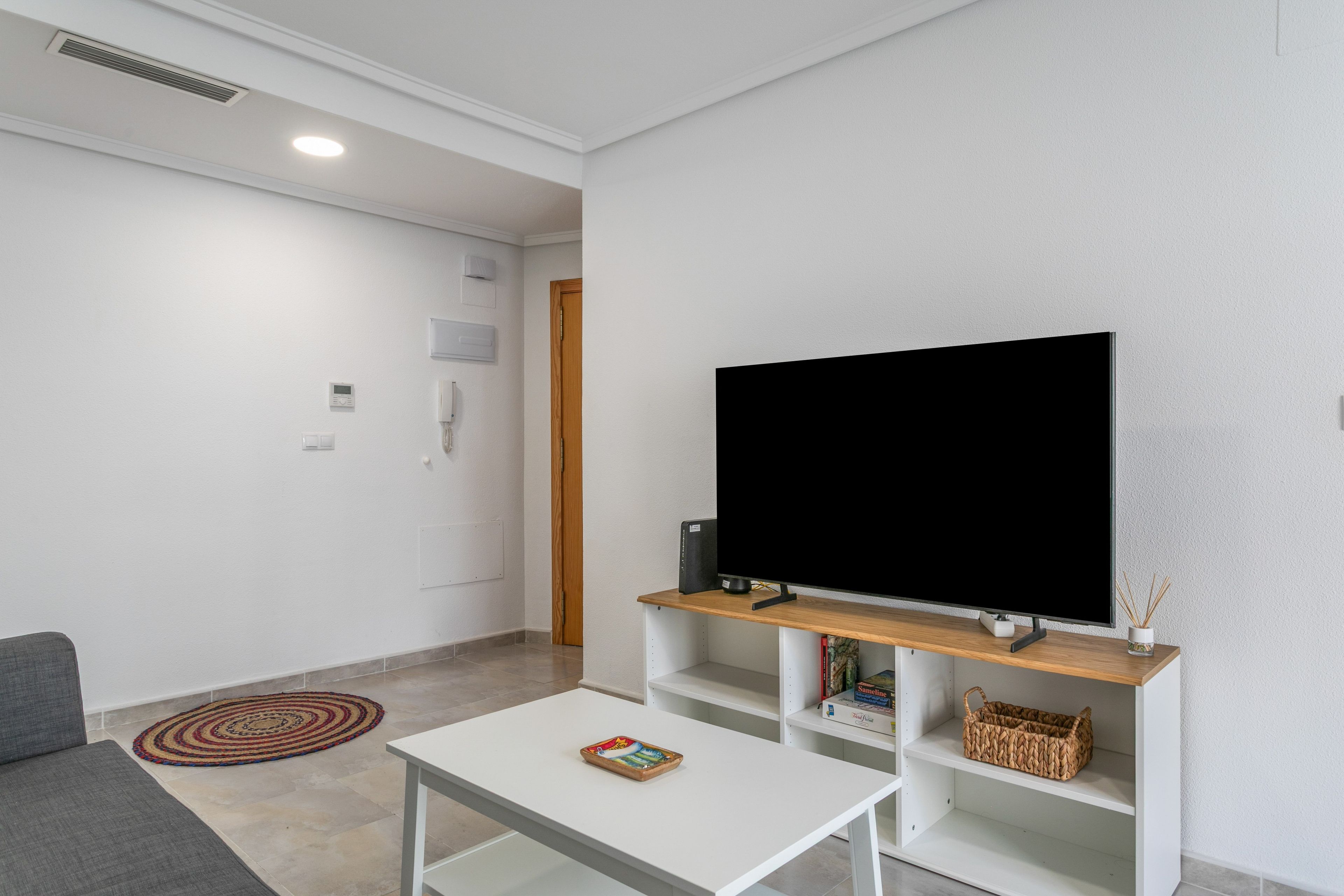 Una sala moderna con un televisor de pantalla plana sobre un mueble de madera, una mesa de centro blanca y un sofá gris.