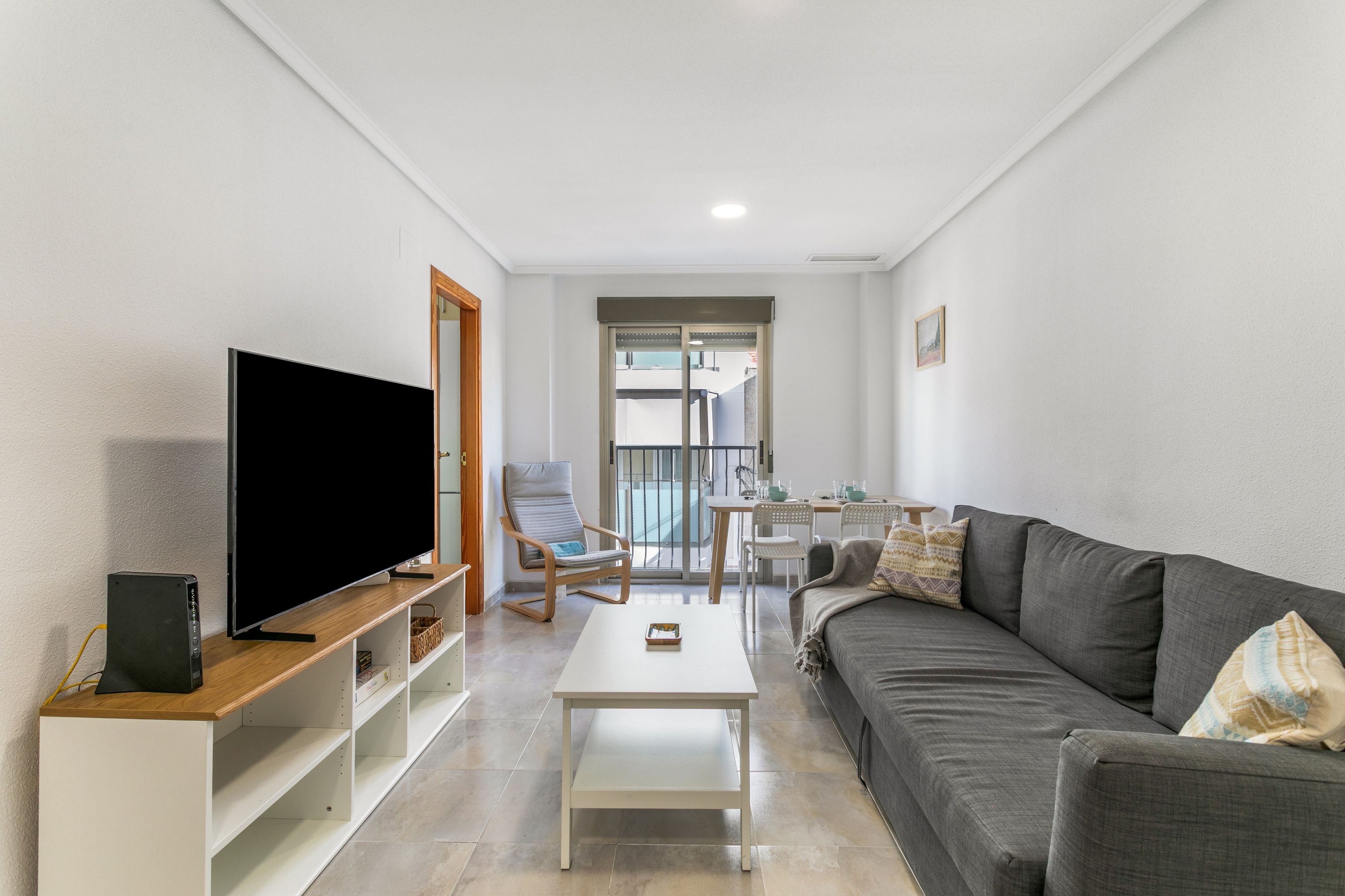 A modern living room with a flat-screen TV, a sofa, a coffee table, and a dining area with chairs and a table.