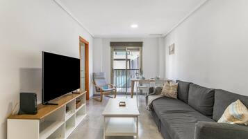 A modern living room with a flat-screen TV, a sofa, a coffee table, and a dining area with chairs and a table.