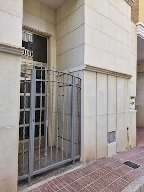 A building facade with a metal gate, a window with a curtain, and a tiled floor. - Holiday Home 'Santa Pola Centro Con Parking' with Balcony, Wi-Fi and Air Conditioning (Santa Pola)
