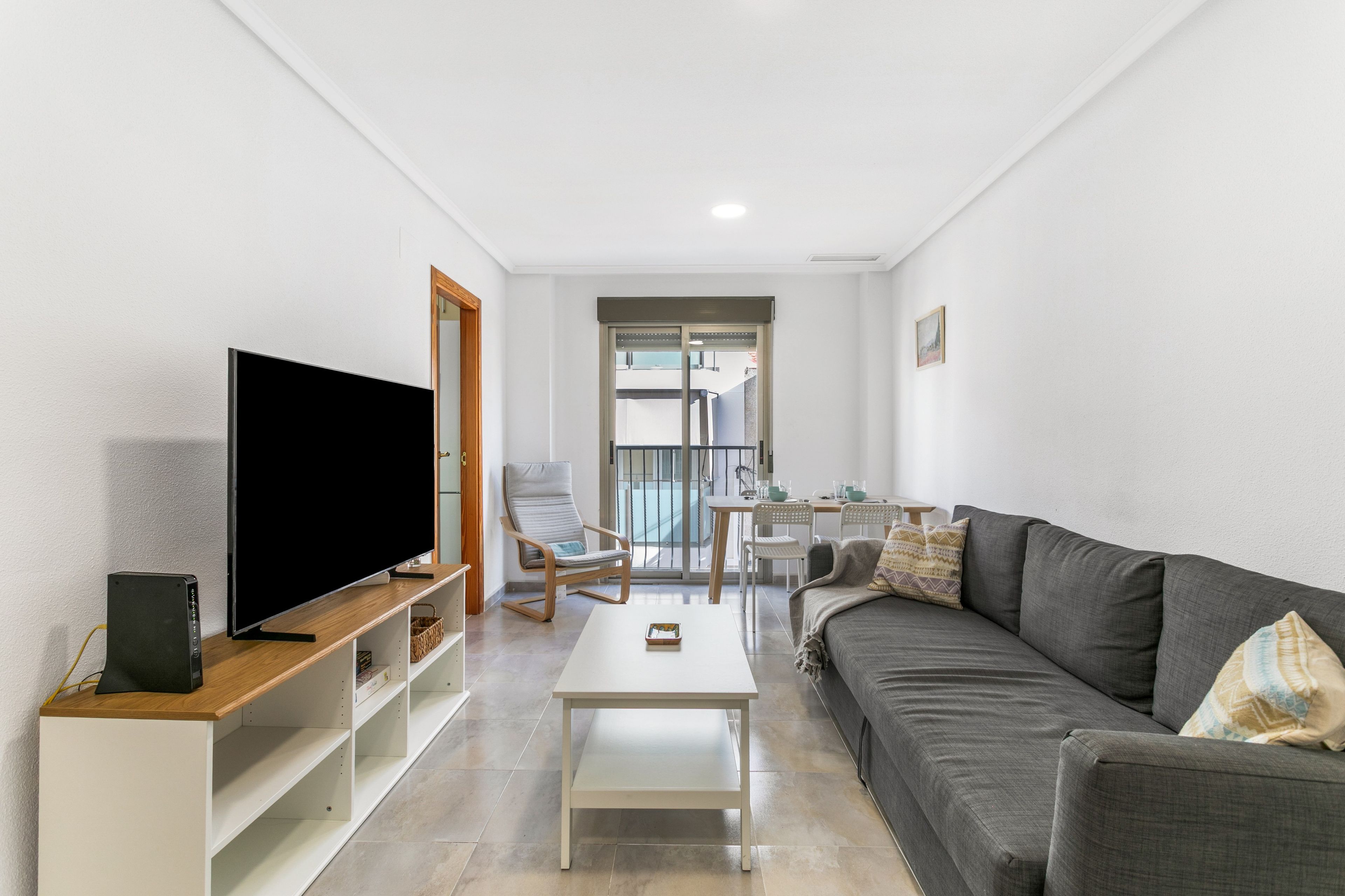 A modern living room with a flat-screen TV, a sofa, a coffee table, and a dining area with chairs and a table.