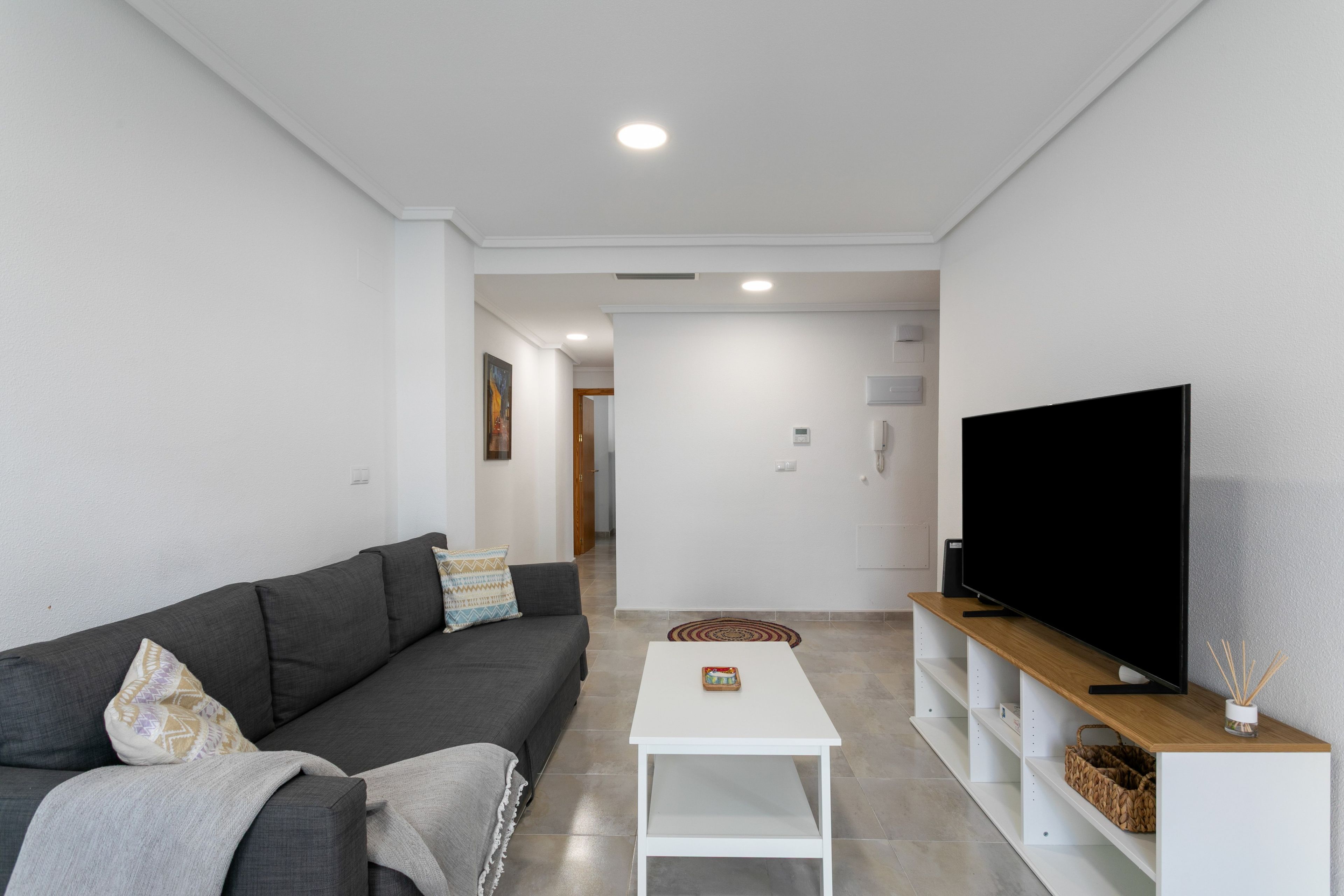 A modern living room with a grey sofa, a white coffee table, and a flat-screen TV on a wooden stand.