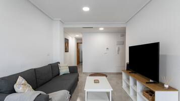 A modern living room with a grey sofa, a white coffee table, and a flat-screen TV on a wooden stand.