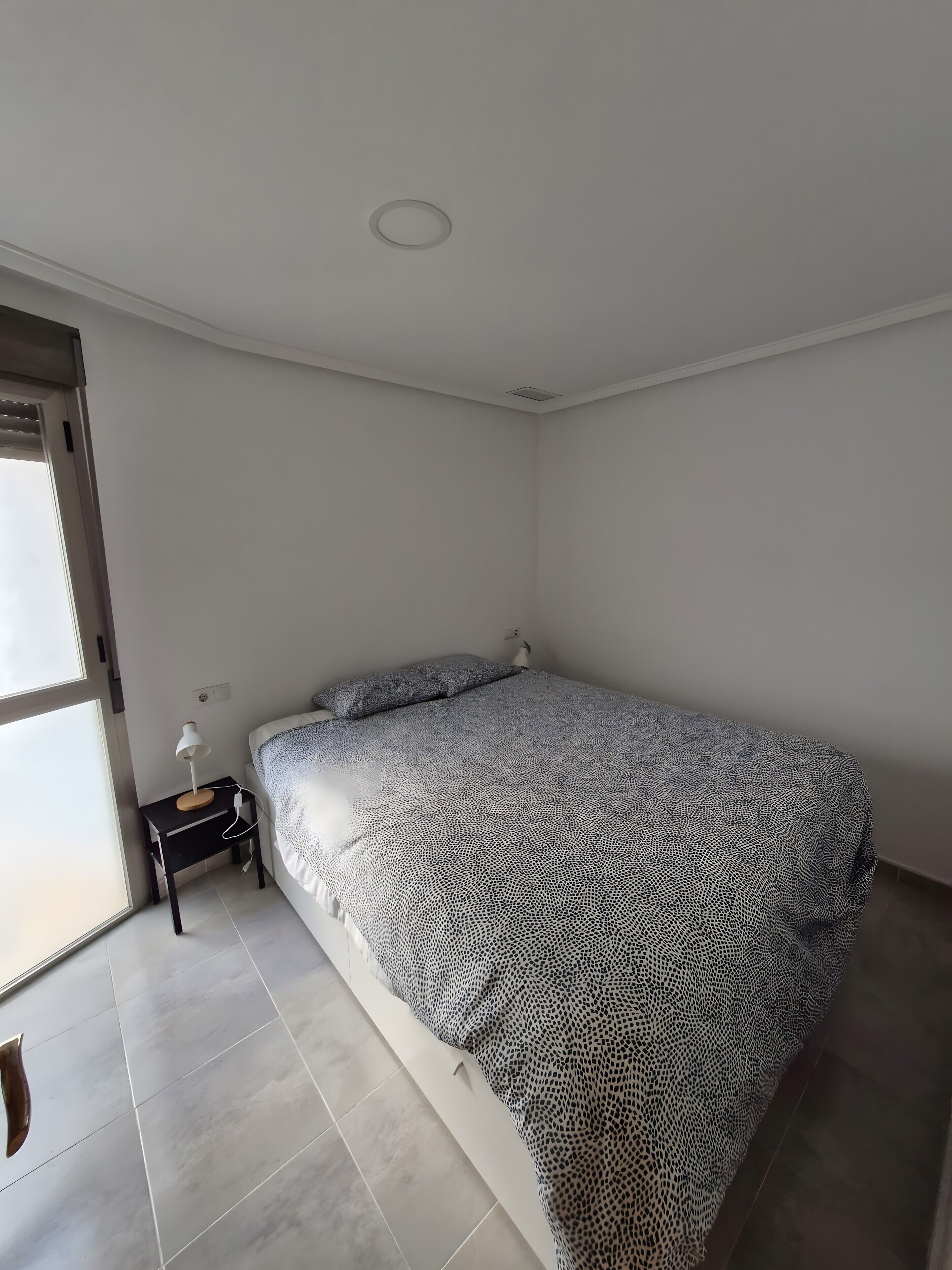 Een slaapkamer met een bed, nachtkastje, lamp en raam.