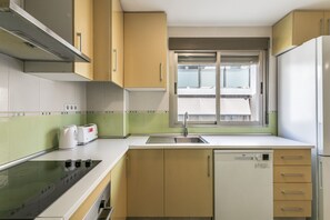 Cocina compacta con lavavajillas integrado, estufa y ventana sobre el fregadero.