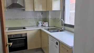 A kitchen with beige cabinets, a stainless steel range hood, a dishwasher, and a window with a view.