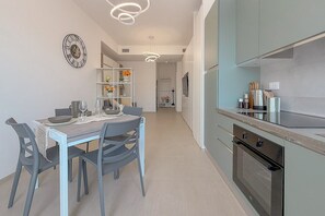 A modern kitchen with a built-in oven, a dining area with a table and chairs, and a decorative wall clock. - Bright Studio with A/C and Balcony (Civitanova Marche)