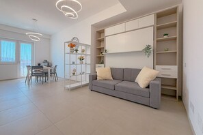 Un salon moderne avec un canapé gris, une table à manger avec des chaises et des étagères intégrées ornées d’objets décoratifs.