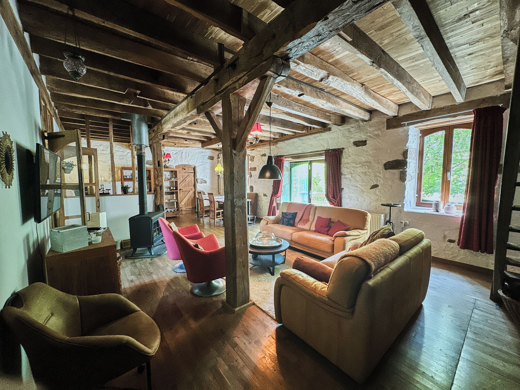 Un interior rústico con vigas de madera a la vista, pared de piedra, chimenea y un rincón de estar acogedor con sofás y sillones.