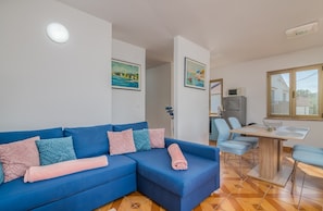 A modern living room with a blue sofa, a dining area with a wooden table and chairs, and artwork on the walls. - Apartment Moderna in Soline (Soline)