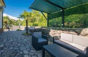 An outdoor patio with stone flooring, a covered seating area with cushions, and a hammock. - Apartment Moderna in Soline (Soline)