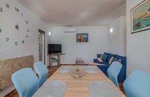 A modern living room with a blue sofa, a dining table with chairs, a TV on a stand, and a painting on the wall. - Apartment Moderna in Soline (Soline)