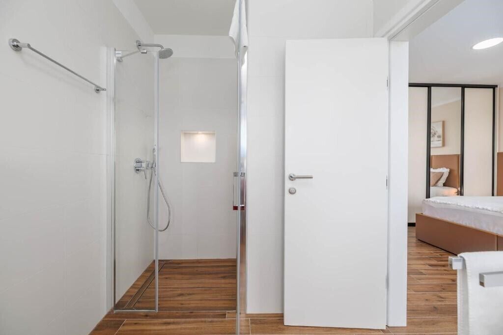 Un bagno moderno con box doccia in vetro, una porta bianca e pavimento in legno.