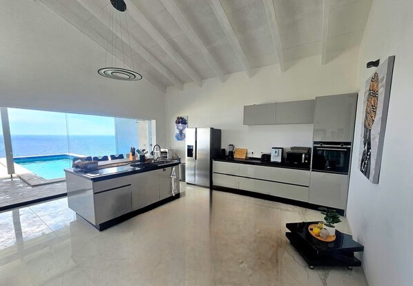A modern kitchen with a view of the ocean, a dining area, and a large window.
