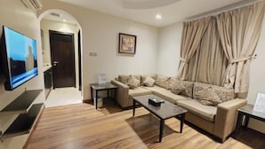 A living room with a sofa, a coffee table, a TV, and a window with curtains. - Dalu Serviced Apartments (Al Khobar)