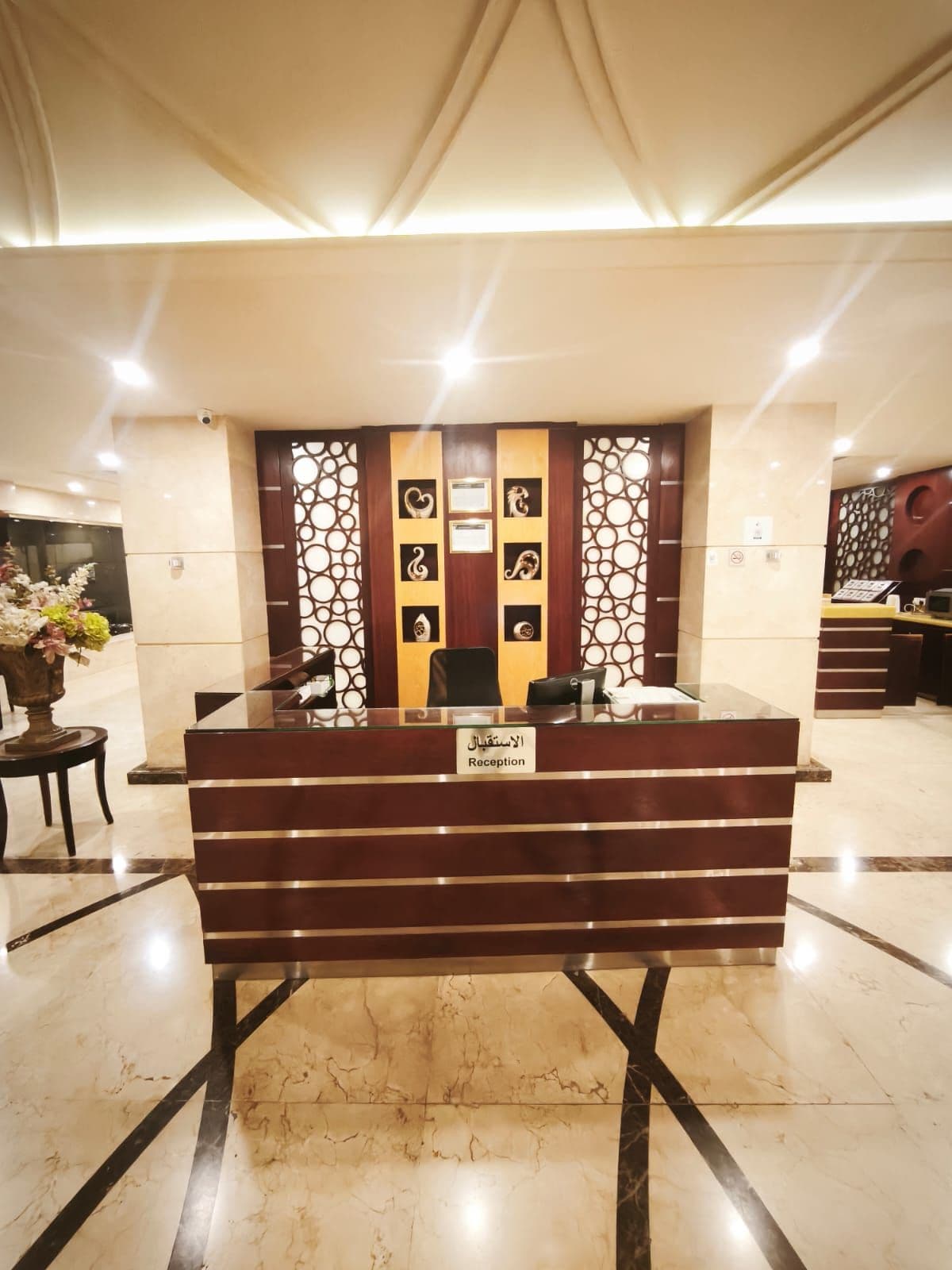 A reception desk with a nameplate, a decorative wall with geometric patterns, and a marble floor.