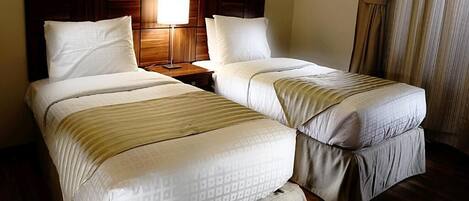 A hotel room with two beds, a wooden headboard, a nightstand with a lamp, and a framed picture on the wall.