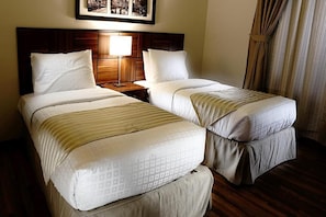 Habitación de hotel con dos camas, cabecera de madera, mesita de noche con lámpara y un cuadro enmarcado en la pared.