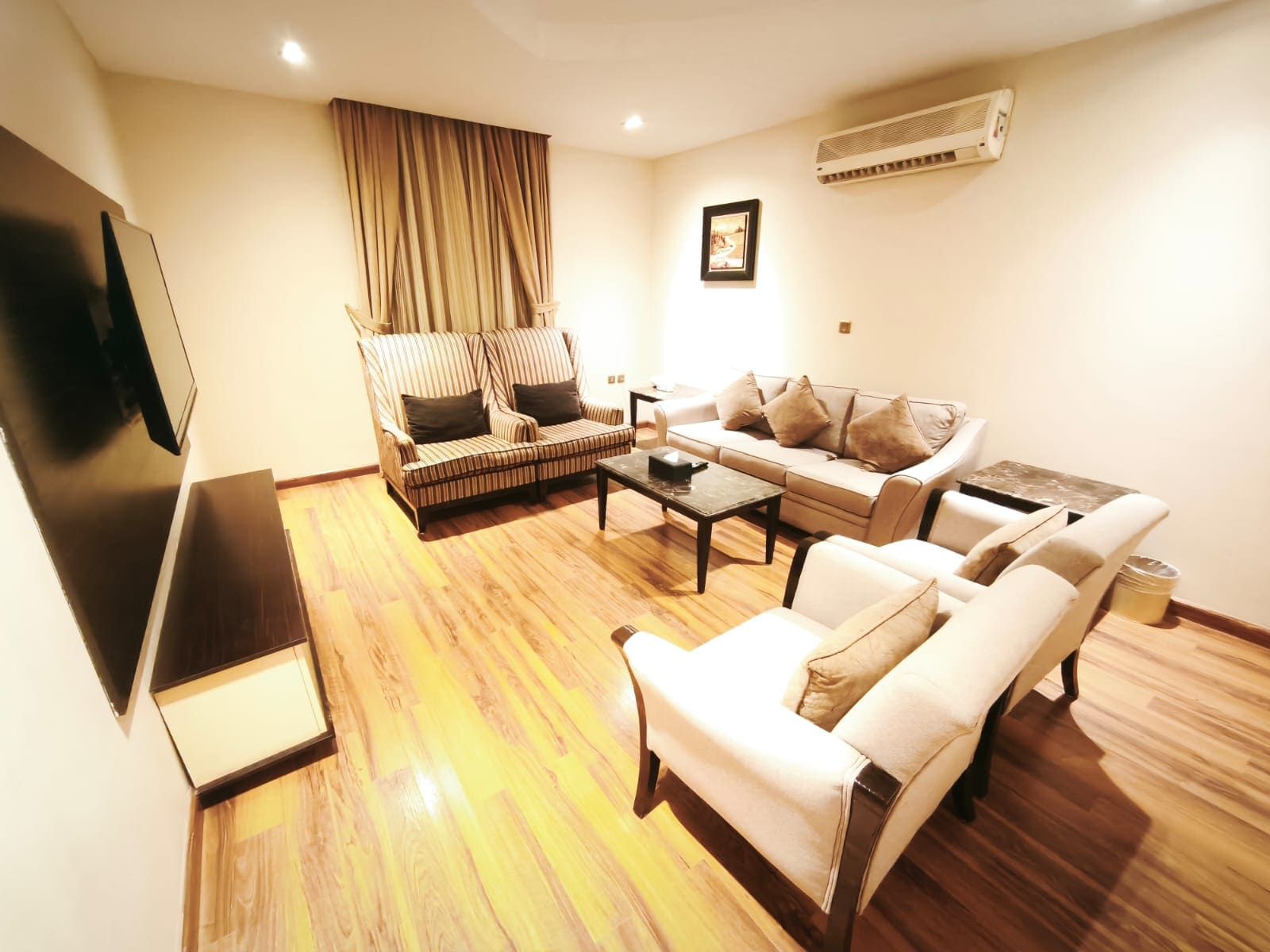 Una sala de estar con sofá, sillones, una mesa de centro y un televisor de pantalla plana.