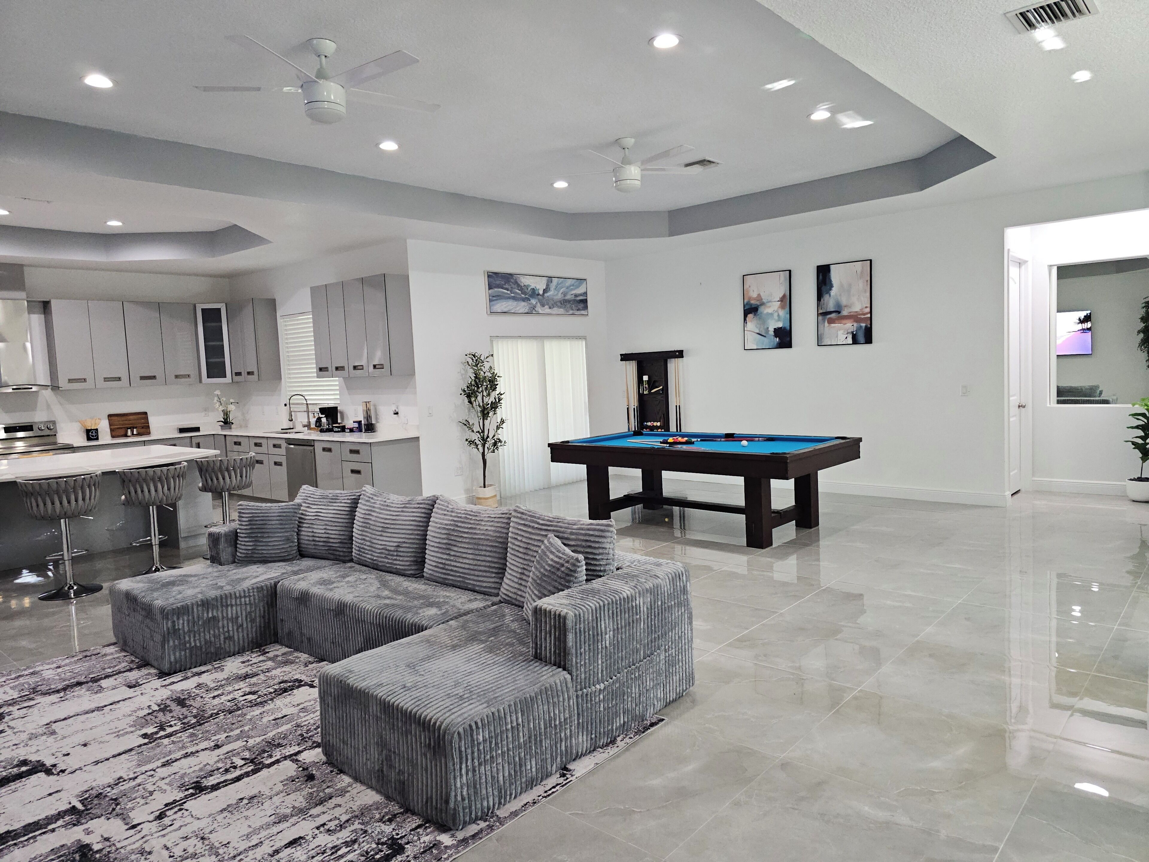 A modern living room with a pool table, grey sectional sofa, and a bar area.