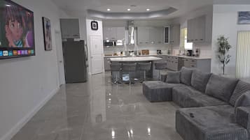 A modern kitchen with a central island, grey upholstered seating, and a flat-screen TV mounted on the wall.