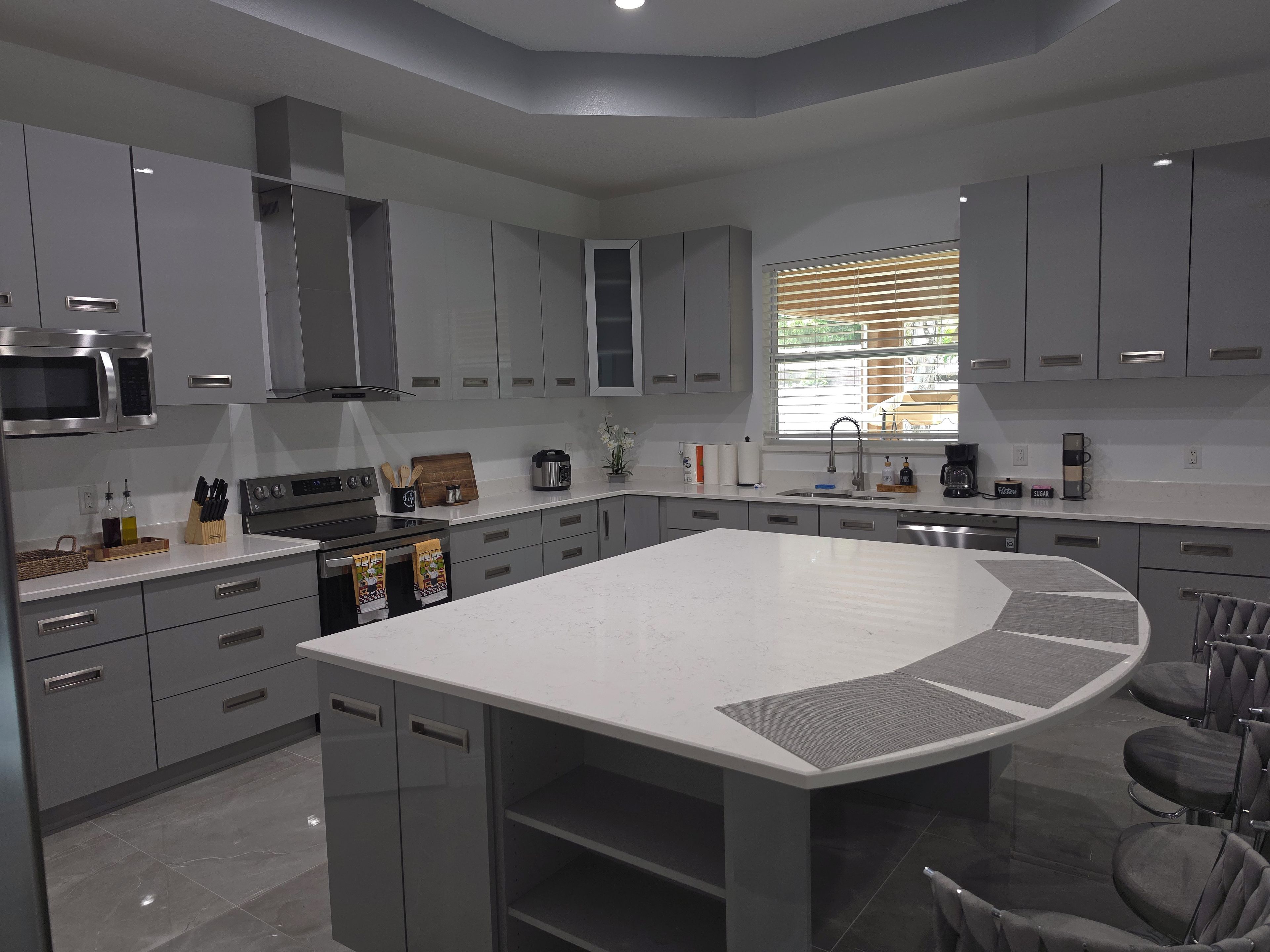 A modern kitchen with grey cabinets, a large island, and a built-in oven.