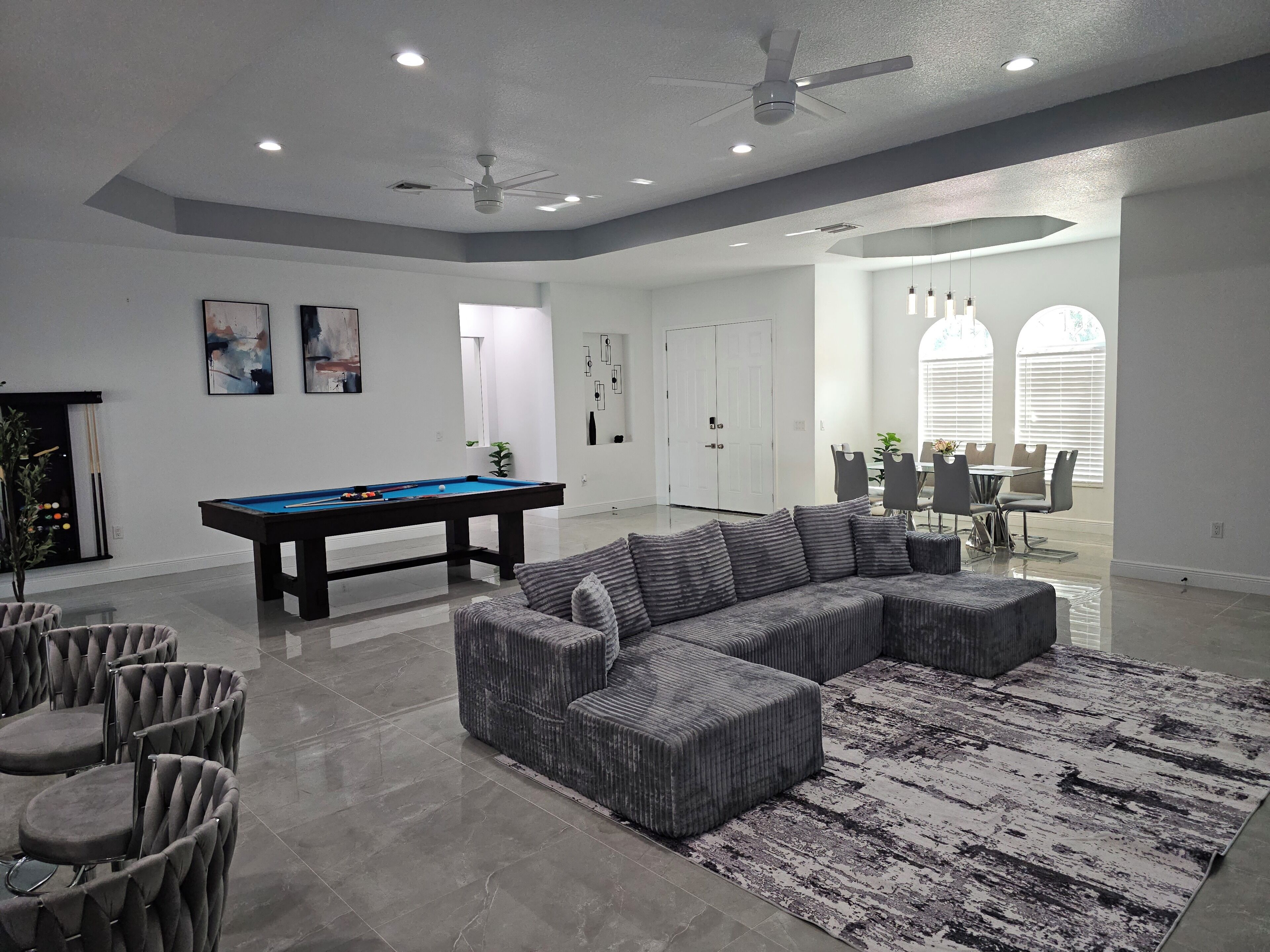 A modern living room with a pool table, a sectional sofa, and a dining area with chairs and a table.