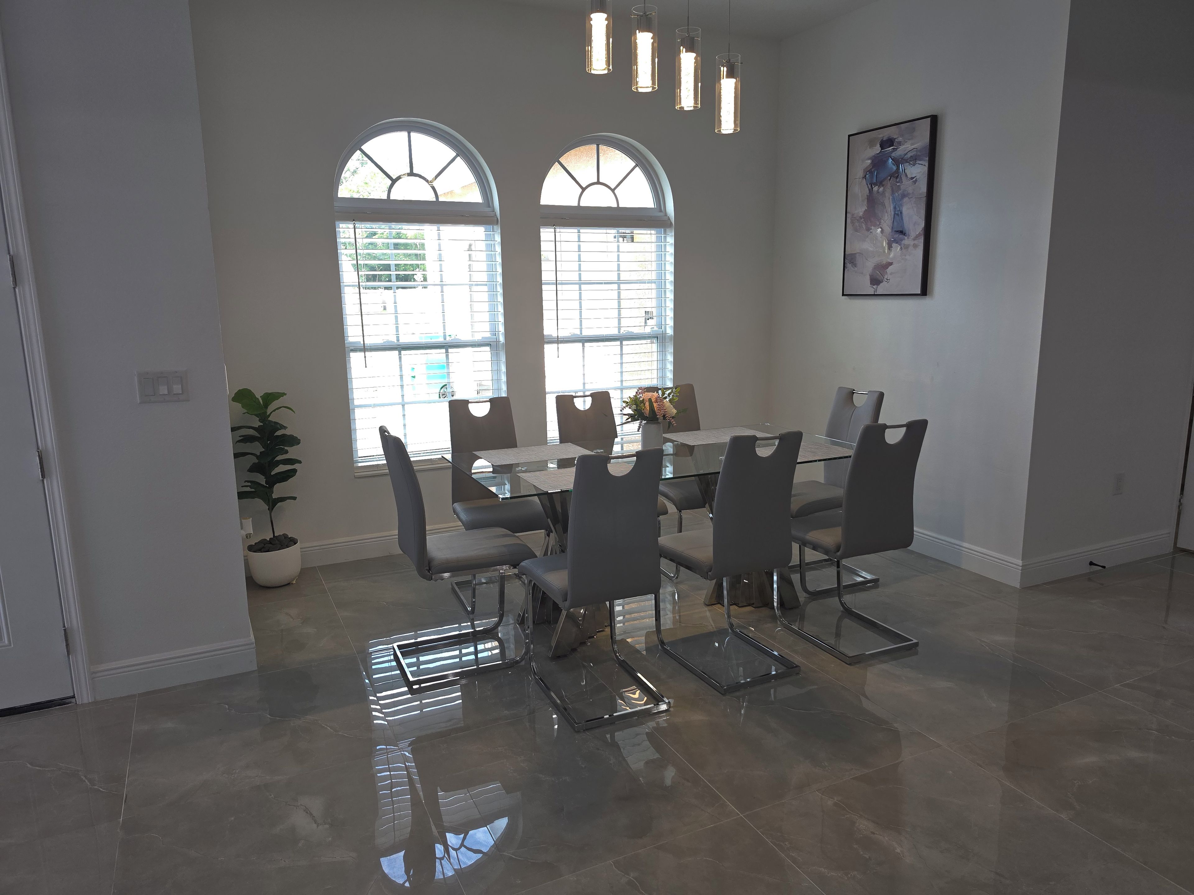 Un comedor con mesa y sillas de vidrio, ventanas amplias e iluminación colgante.