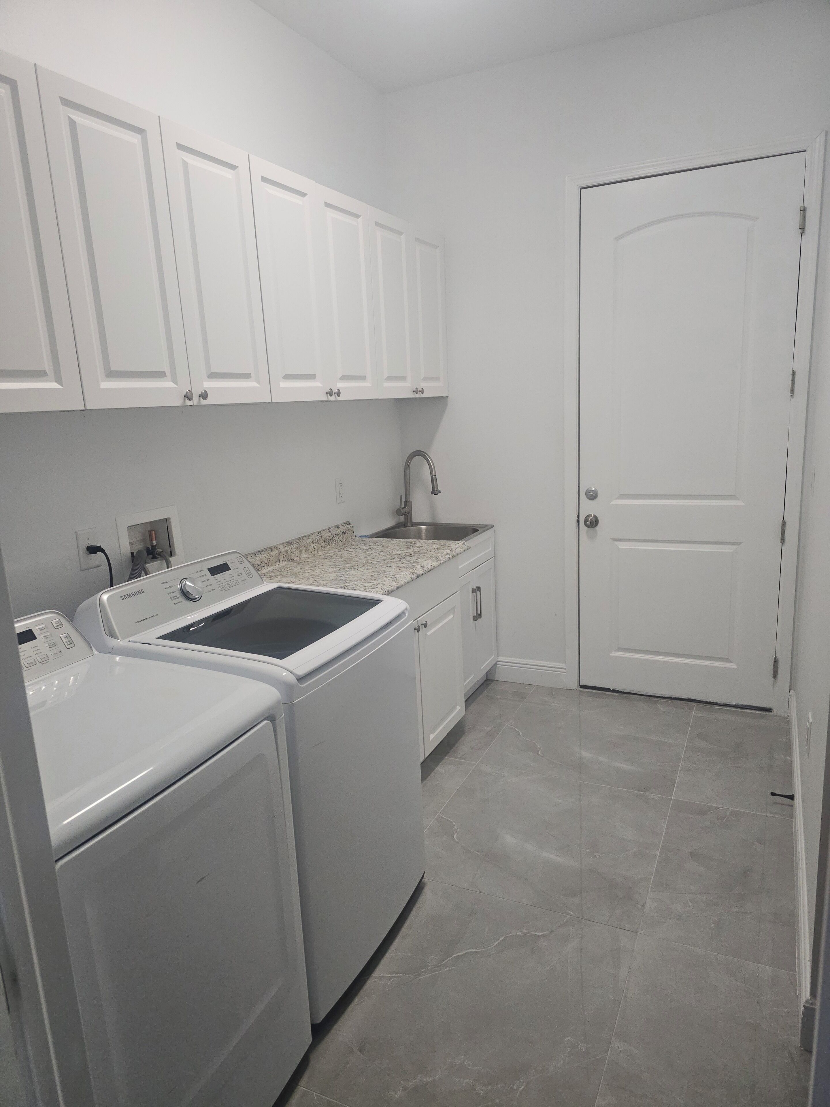 A laundry area with a washing machine and dryer, a sink, and a door.