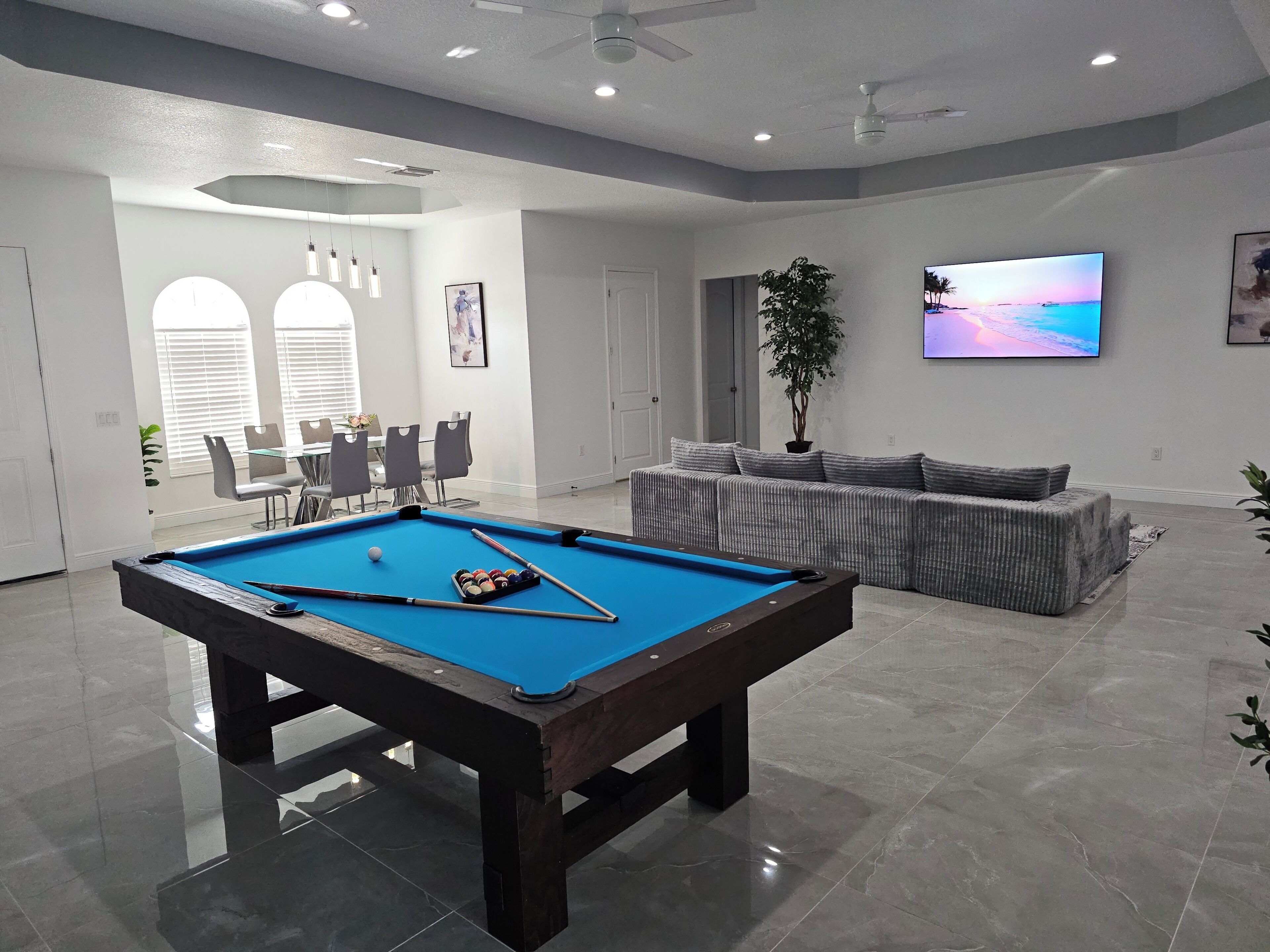 A modern living room with a pool table, a sofa, a TV, and a dining area.