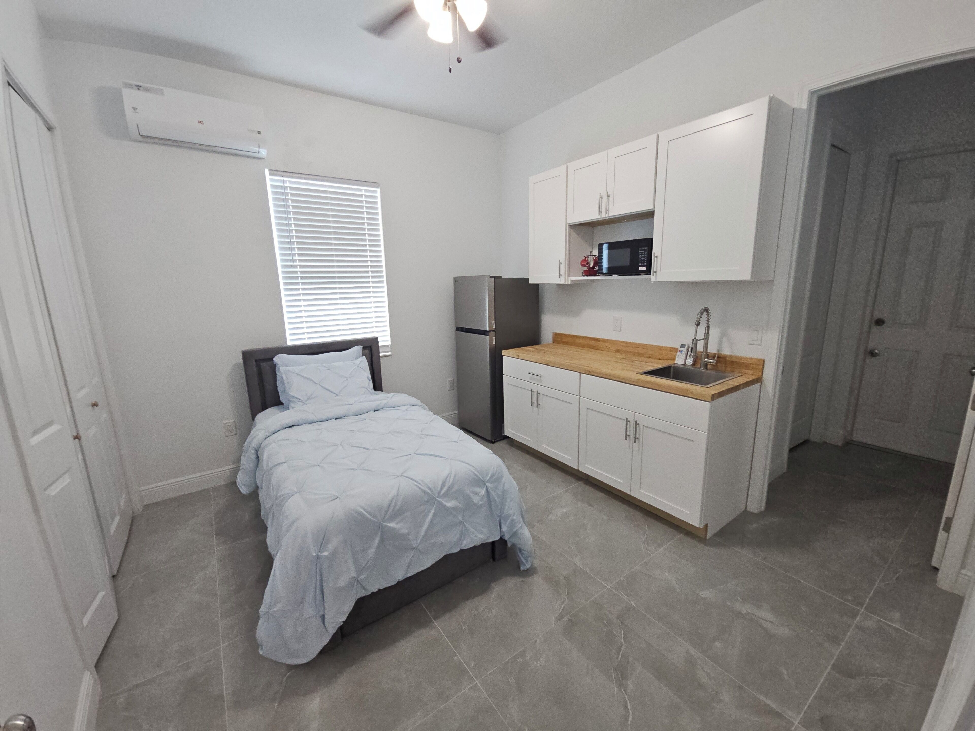 A compact bedroom with a bed, a small kitchenette, and a bathroom.