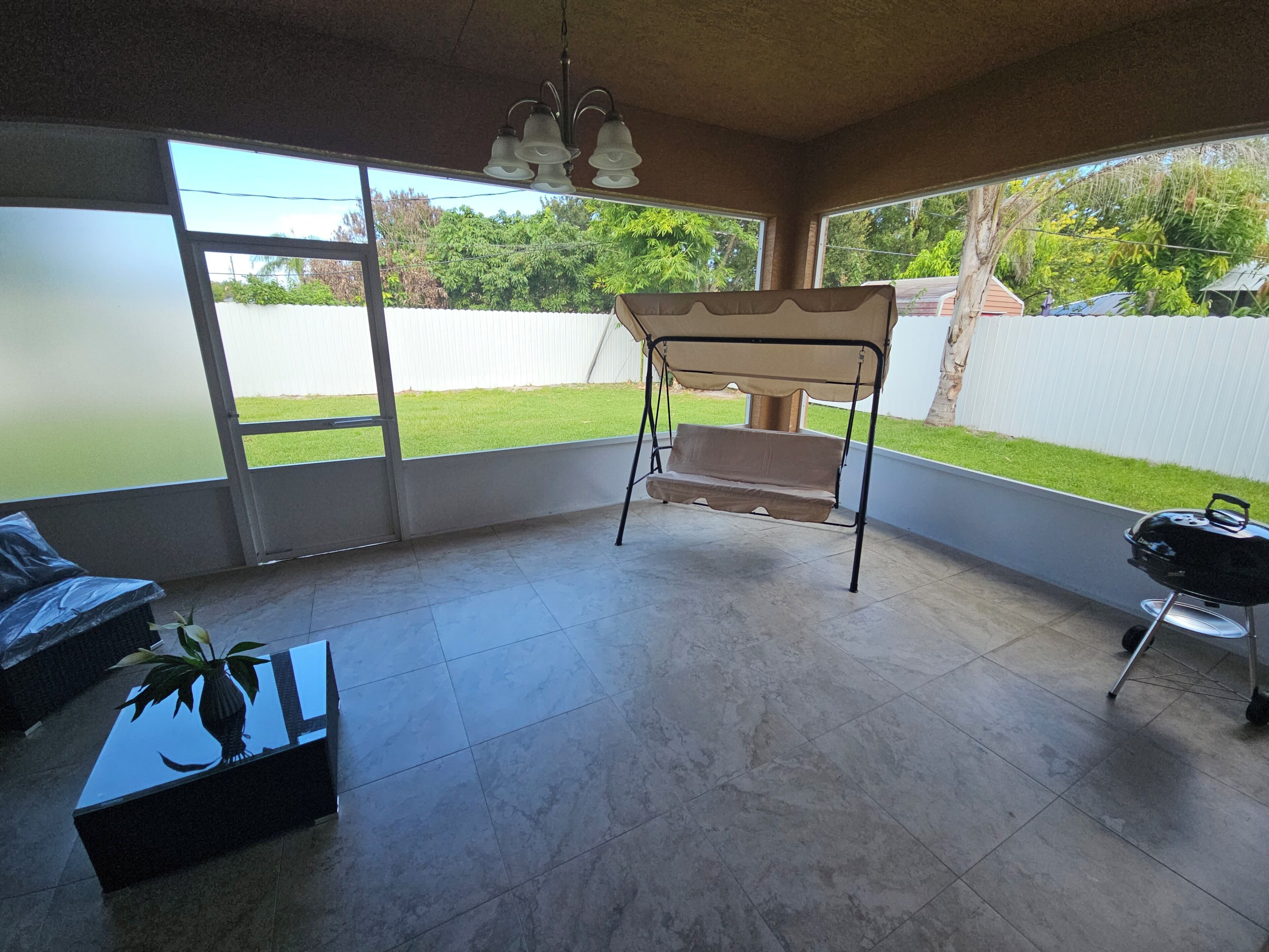 A room with a swing chair, a grill, and a view of a green lawn.
