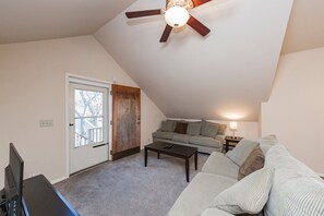 En stue med loftventilator, sofa, sofabord og en dør til en balkon.