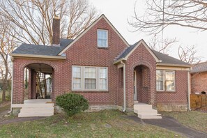 A two-story brick house with a gabled roof, a front entrance with a door, and a small front yard with a bush. - 2 Bedroom Upstairs Apartment in Middle of Nashville! (Nashville)
