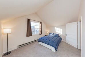 A bedroom with a sloped ceiling, a bed with a blue patterned bedspread, a standing lamp, and a window with curtains. - 2 Bedroom Upstairs Apartment in Middle of Nashville! (Nashville)