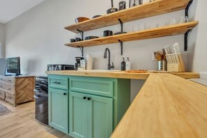 Une cuisine moderne avec des étagères en bois, un meuble vert et un plan de travail en bois.