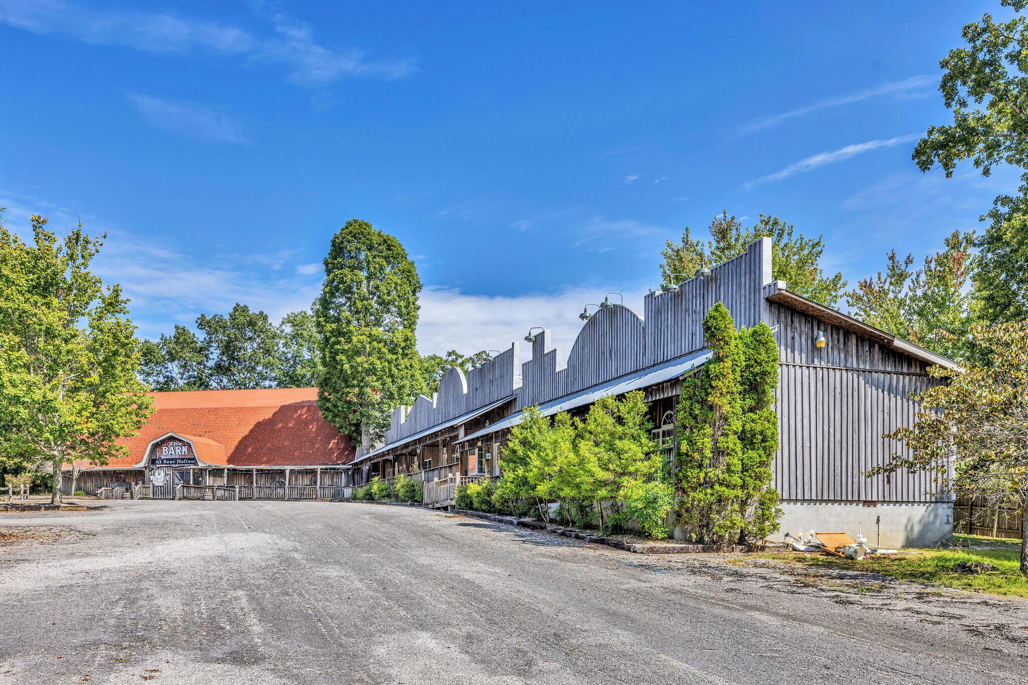 A rustic barn-style building with a red roof, surrounded by trees and a gravel driveway.