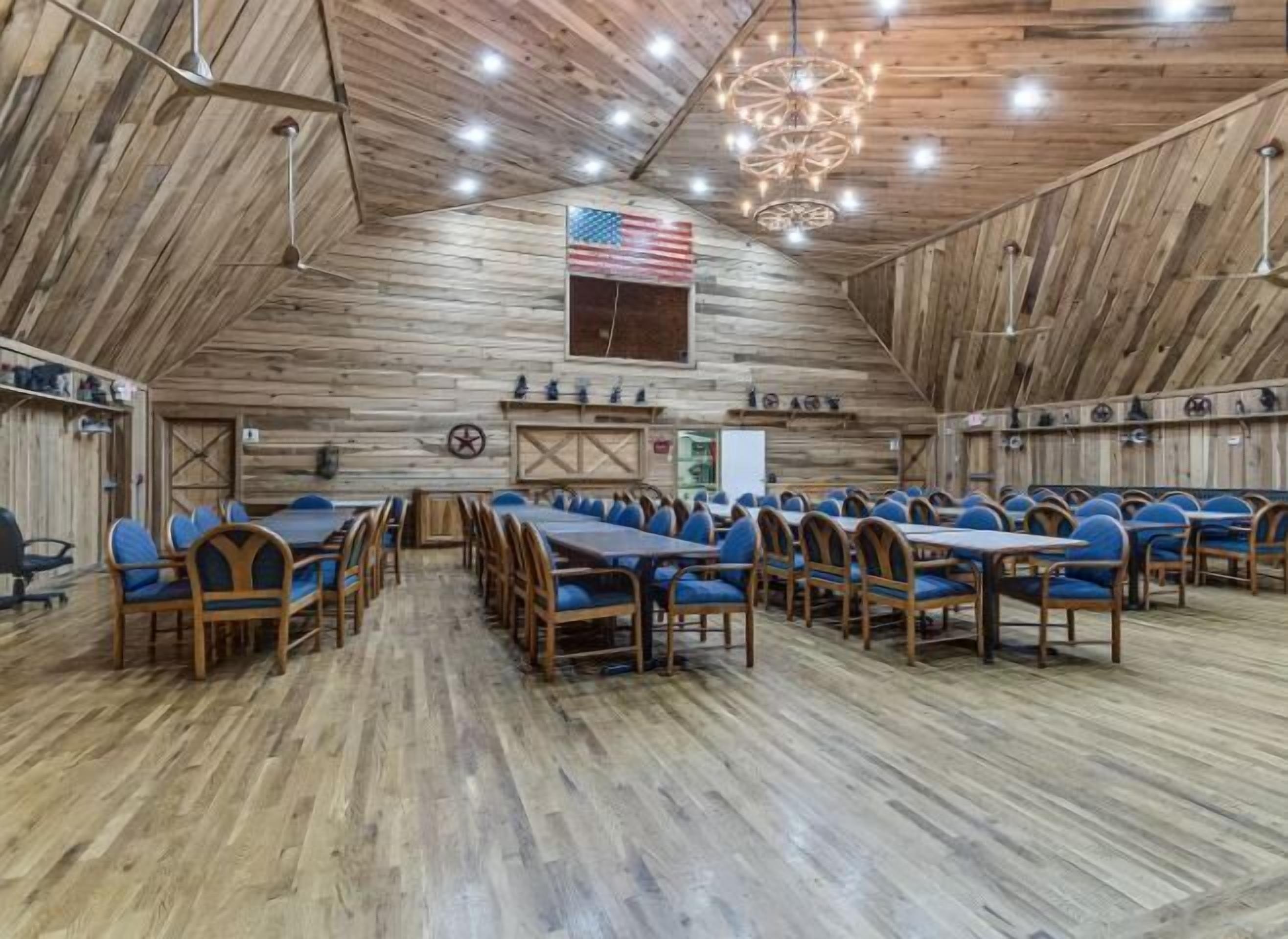A large hall with wooden walls and ceiling, featuring tables and chairs arranged for dining.