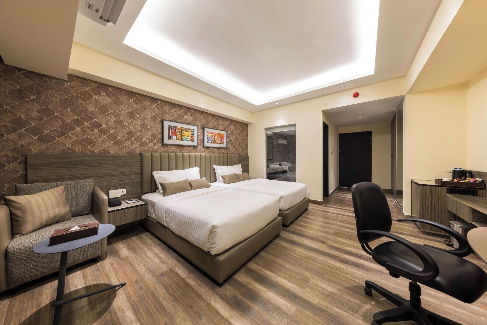 A hotel room with a bed, a desk, a chair, and a bathroom visible through a glass door.