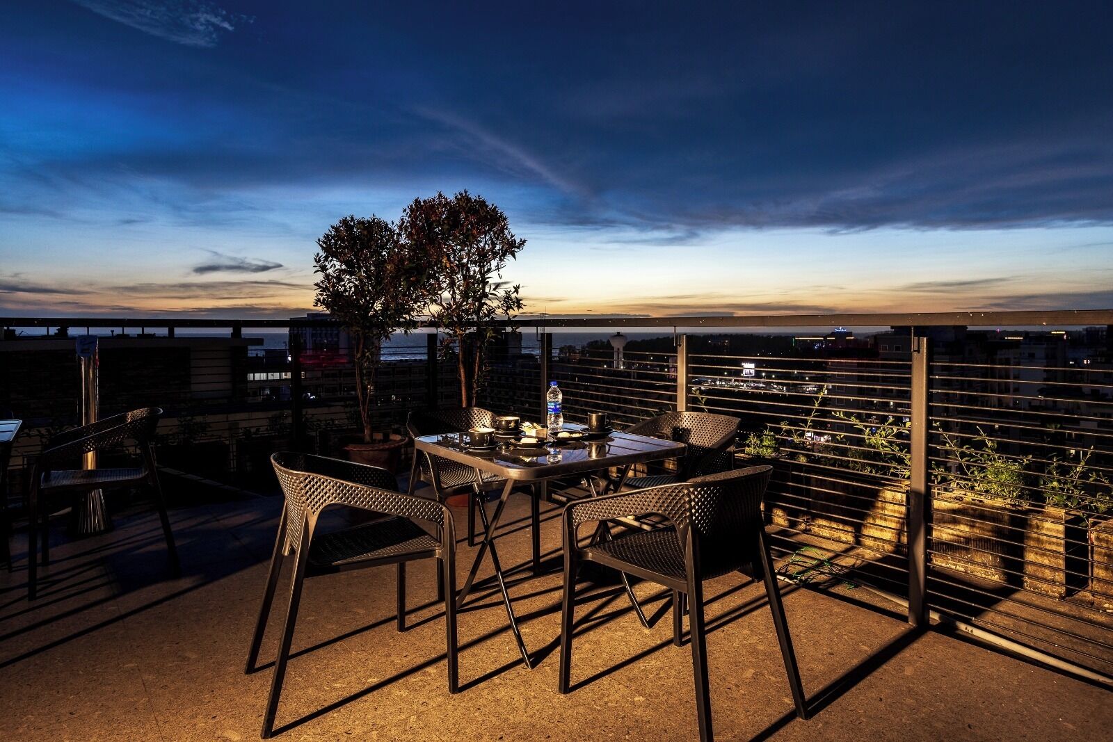 Terraza en la azotea con una mesa, sillas, plantas en macetas y vistas de la ciudad.