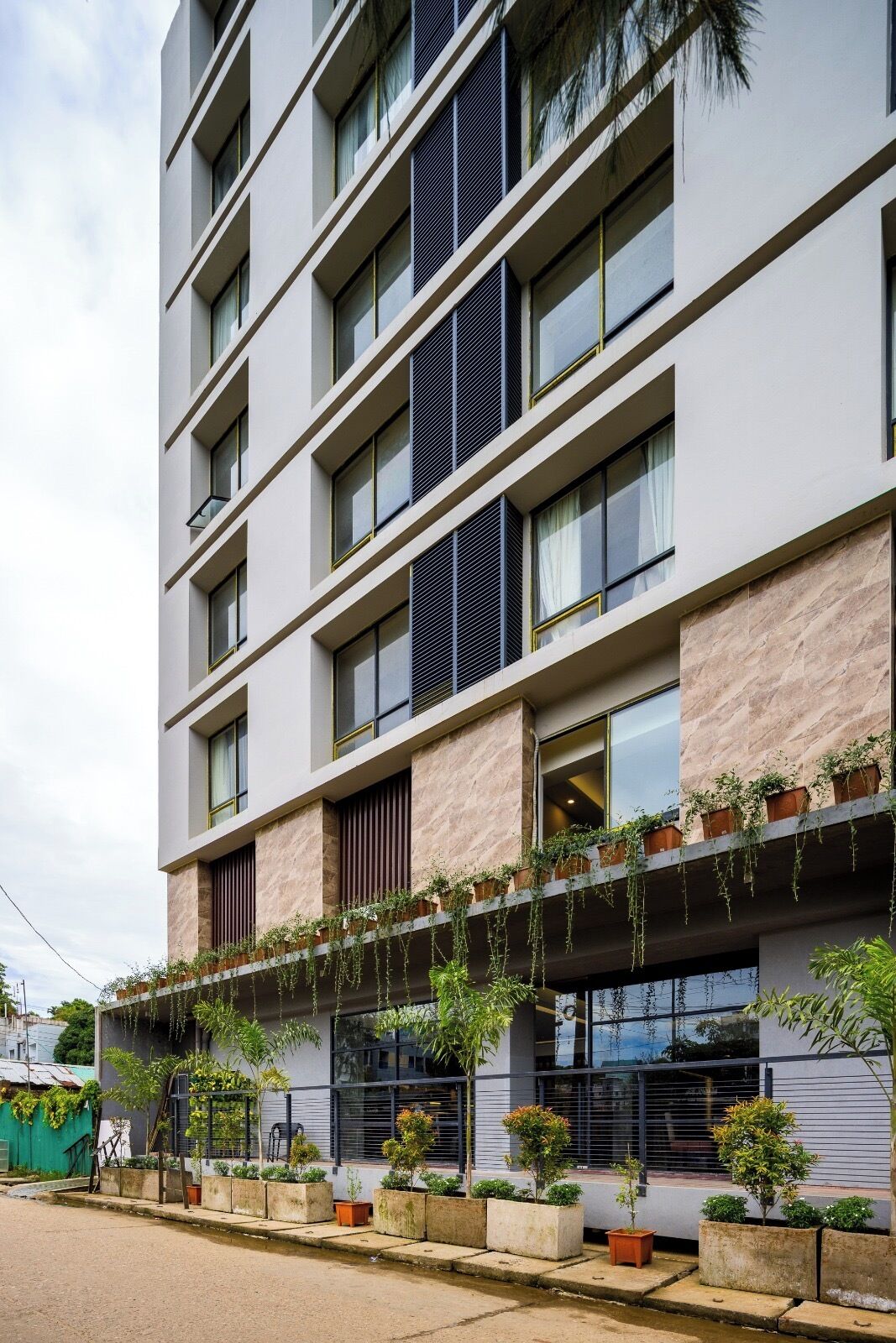 Un edificio moderno de varios pisos, con balcones decorados con plantas en macetas y una fachada limpia y estructurada.