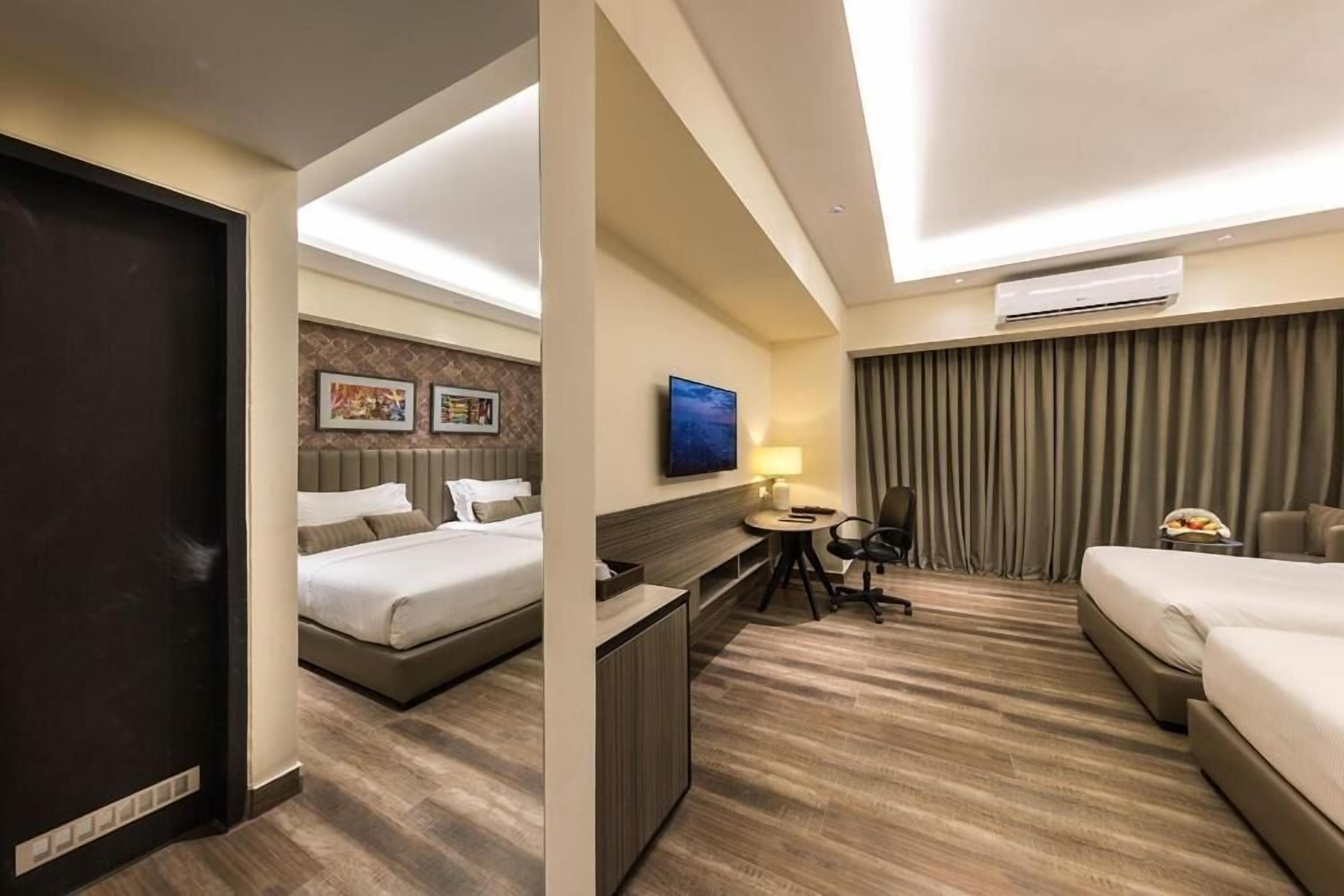 A hotel room with a bed, a desk, a chair, a TV, and an air conditioning unit.