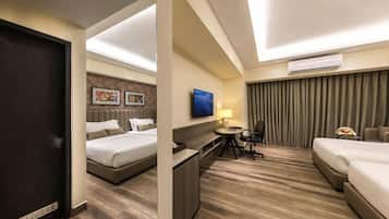 A hotel room with a bed, a desk, a chair, a TV, and an air conditioning unit.