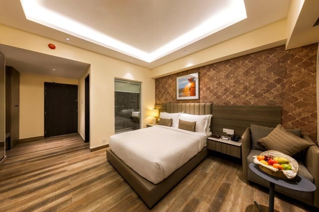 A hotel room with a large bed, a bedside table with a lamp, a small sofa, and a fruit basket.